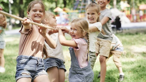 Kinder spielen gemeinsam Tauziehen auf einem Spielplatz im Freien.